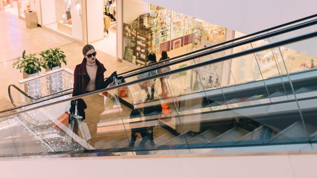 A stylish-looking woman rides an escalator in a shopping mall